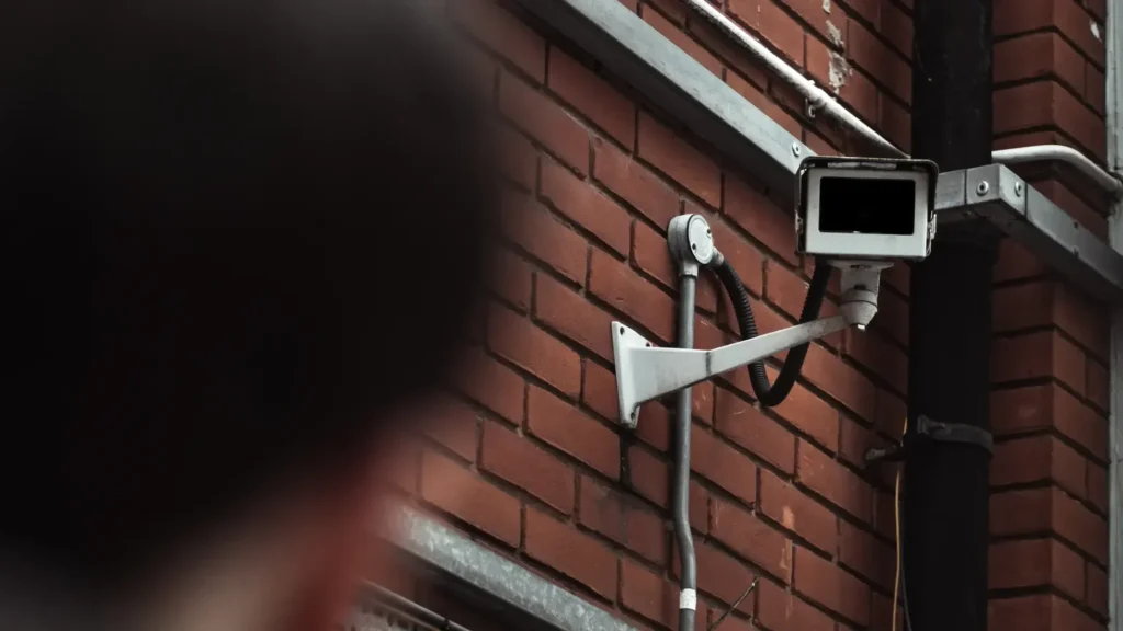 Baltos lauko stebėjimo kameros ant brick sienos su matomu laikikliu ir laidais.